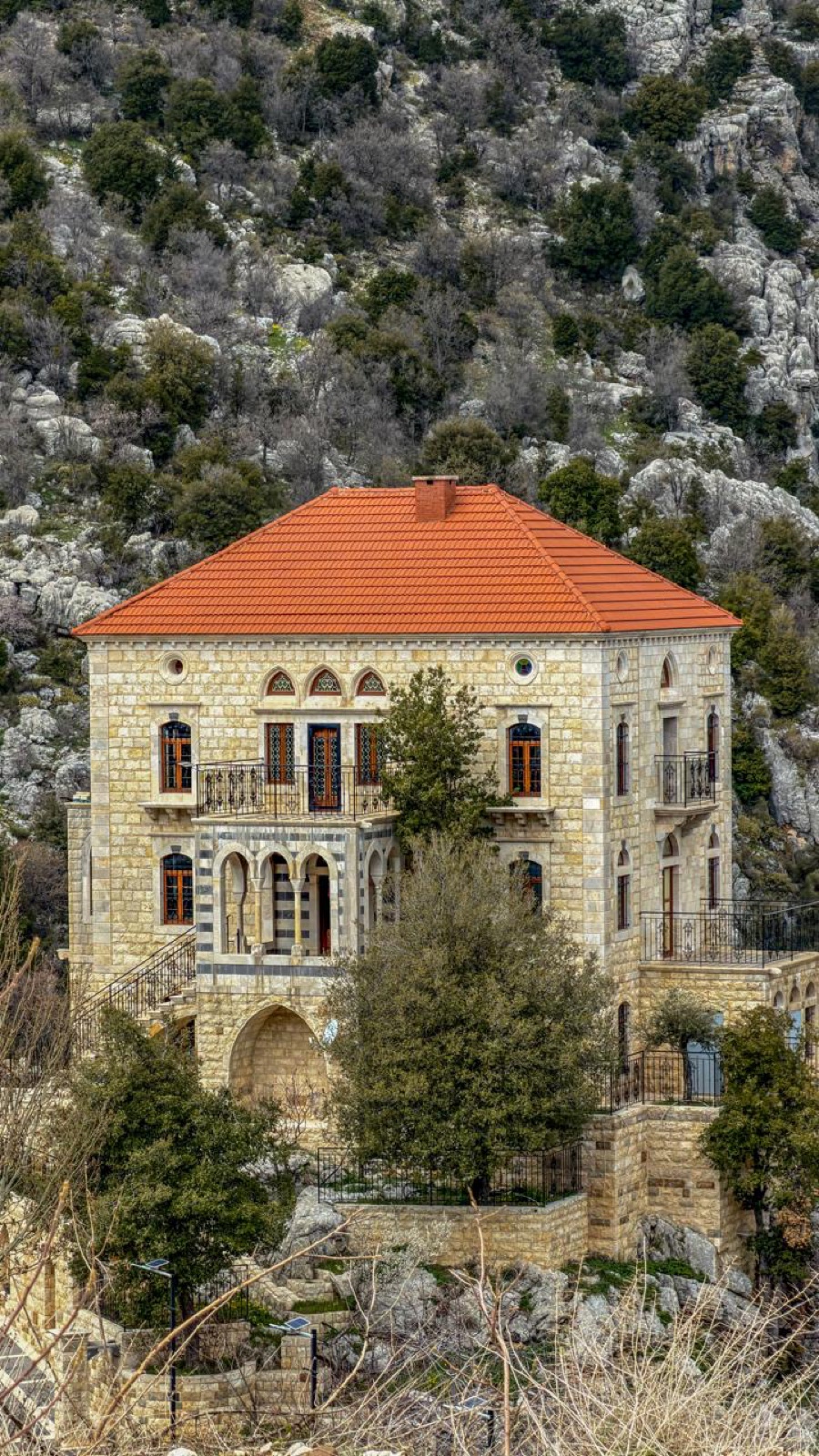 Traditional Lebanese stone house with a red tiled roof against the mountains