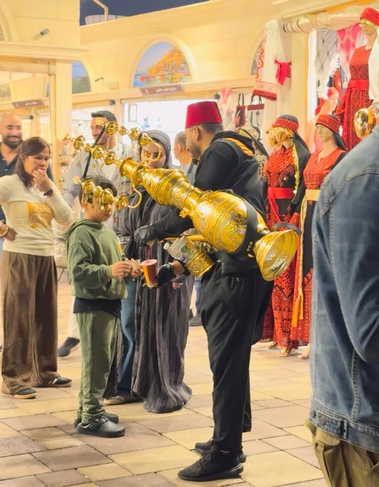 Street seller in a red fez pouring a drink from a golden jug for a child