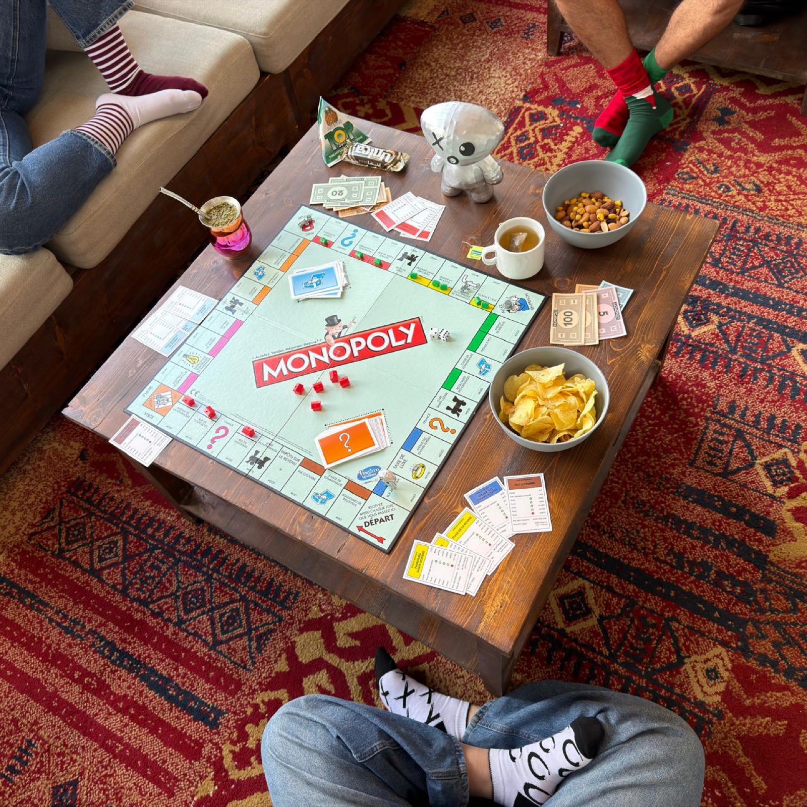 Friends around a coffee table with a Monopoly game, maté, tea and snacks