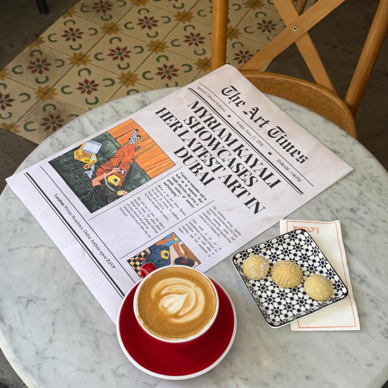 The Art Times newspaper featuring Myriam Kayali's art, next to a cappuccino and maamoul